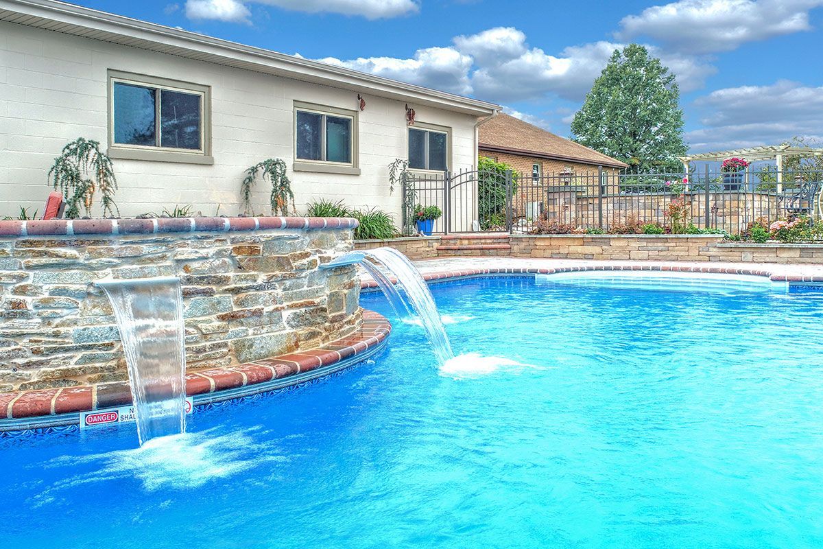 A large swimming pool with a waterfall and a house in the background.