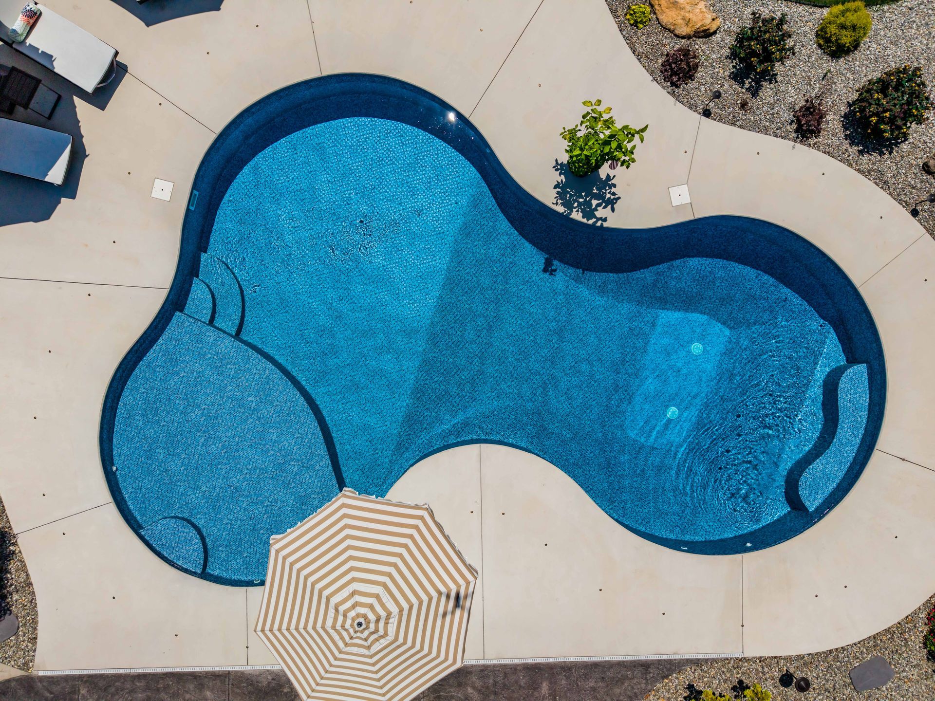 An aerial view of a large swimming pool with a striped umbrella in the middle.