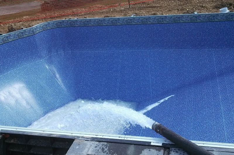 A person is cleaning a swimming pool with a hose.