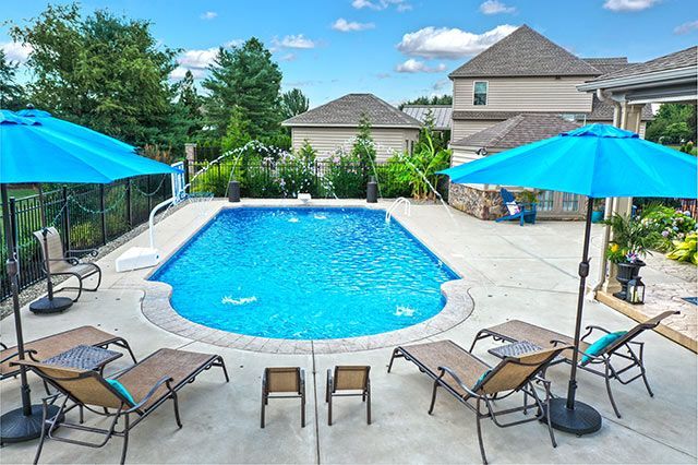 A large swimming pool surrounded by chairs and umbrellas in a backyard.