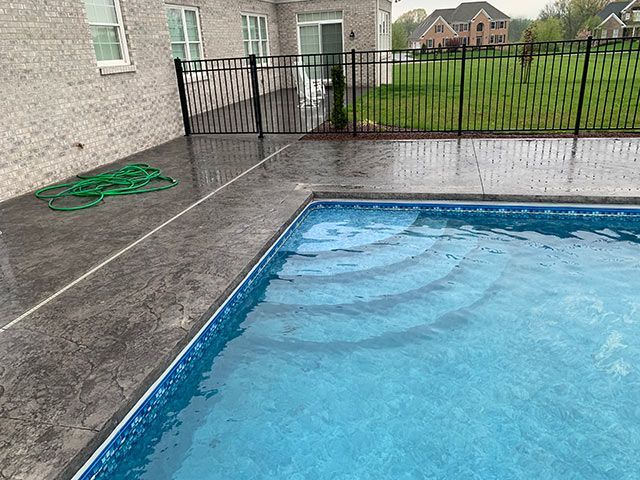 A swimming pool is surrounded by a fence and a brick house.
