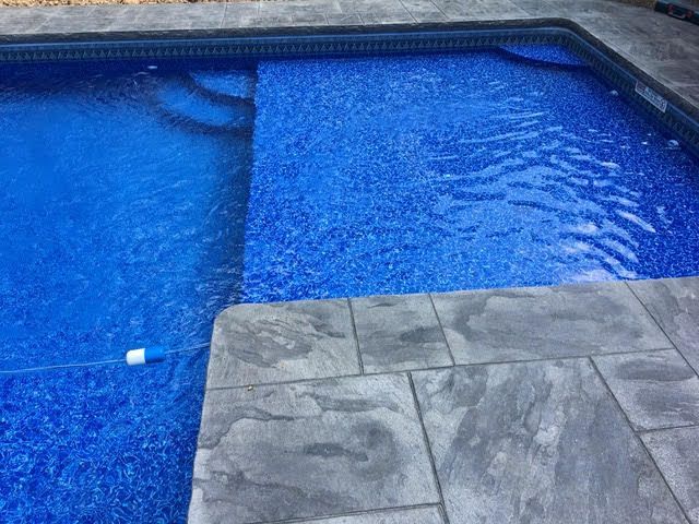 A blue swimming pool with a gray tiled patio in front of it.