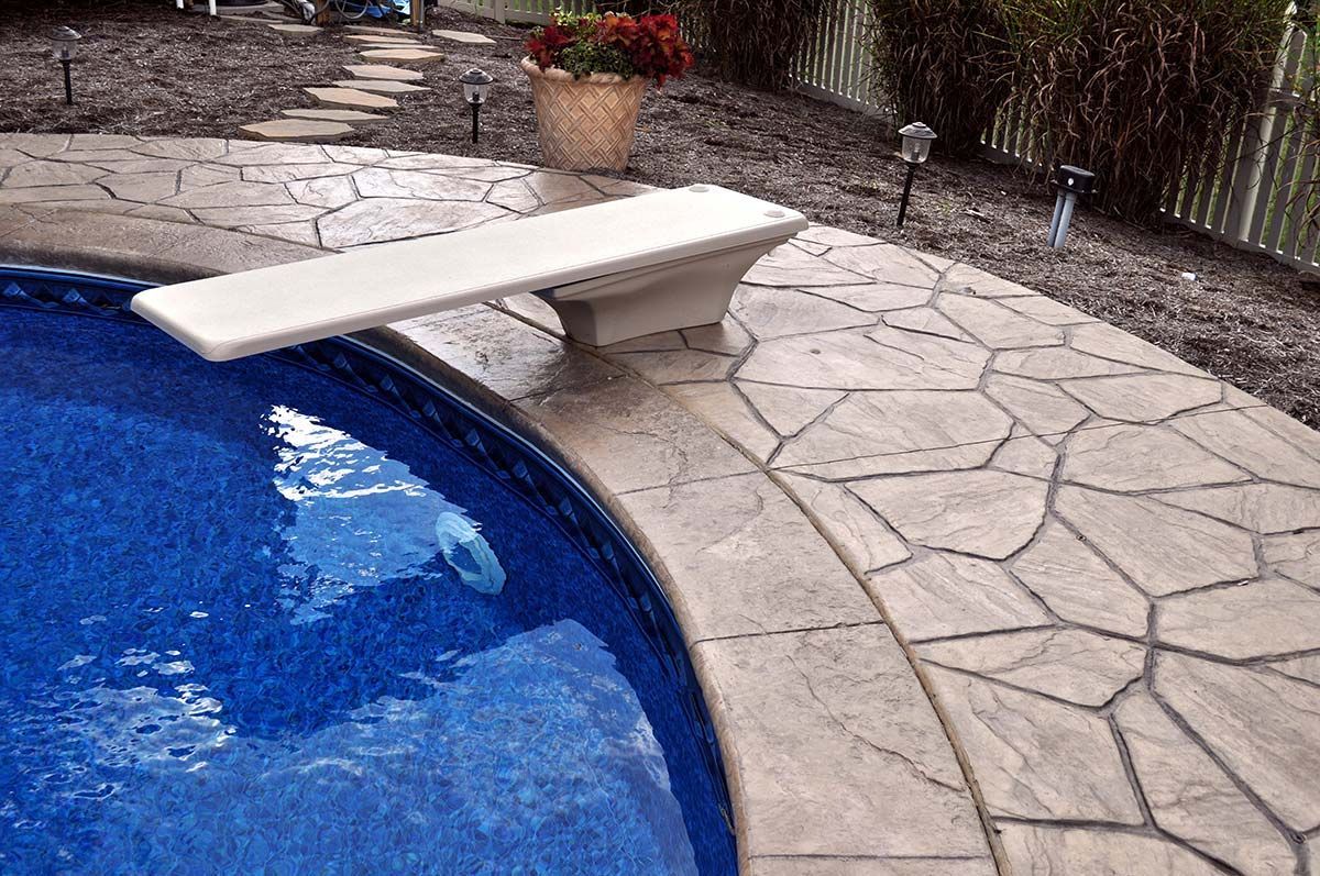 A diving board is sitting next to a swimming pool.