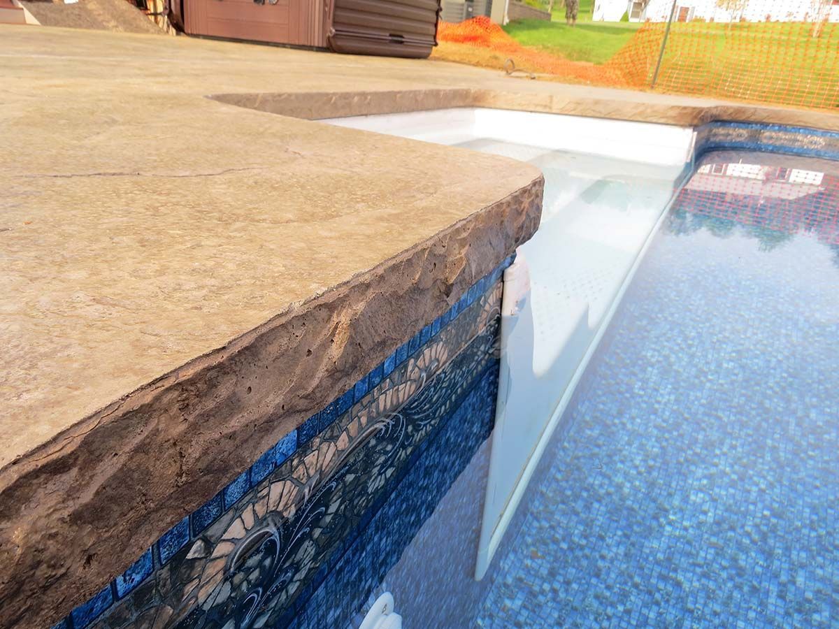 A swimming pool with a concrete ledge and a hot tub in the background.