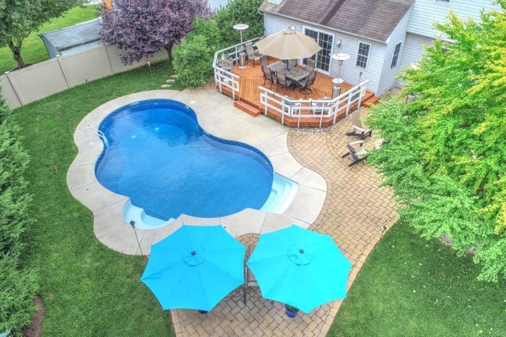 An aerial view of a backyard with a large swimming pool and two blue umbrellas.