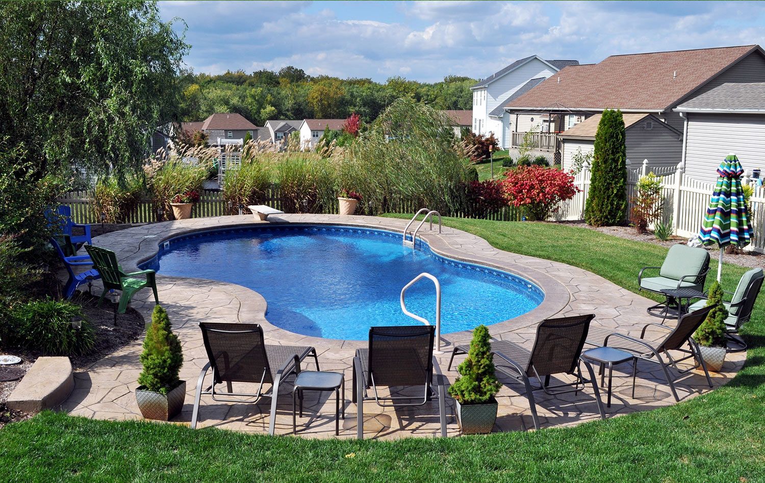 A large swimming pool surrounded by chairs and tables in a backyard.