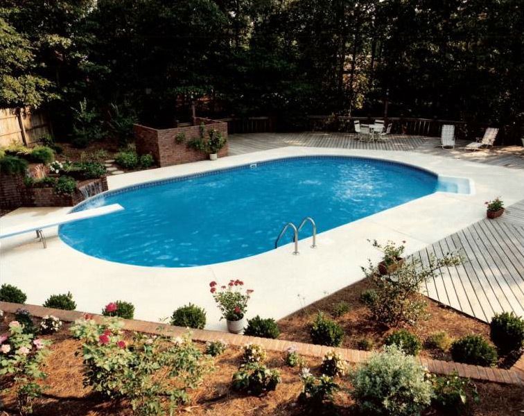 A large oval shaped swimming pool surrounded by flowers and trees