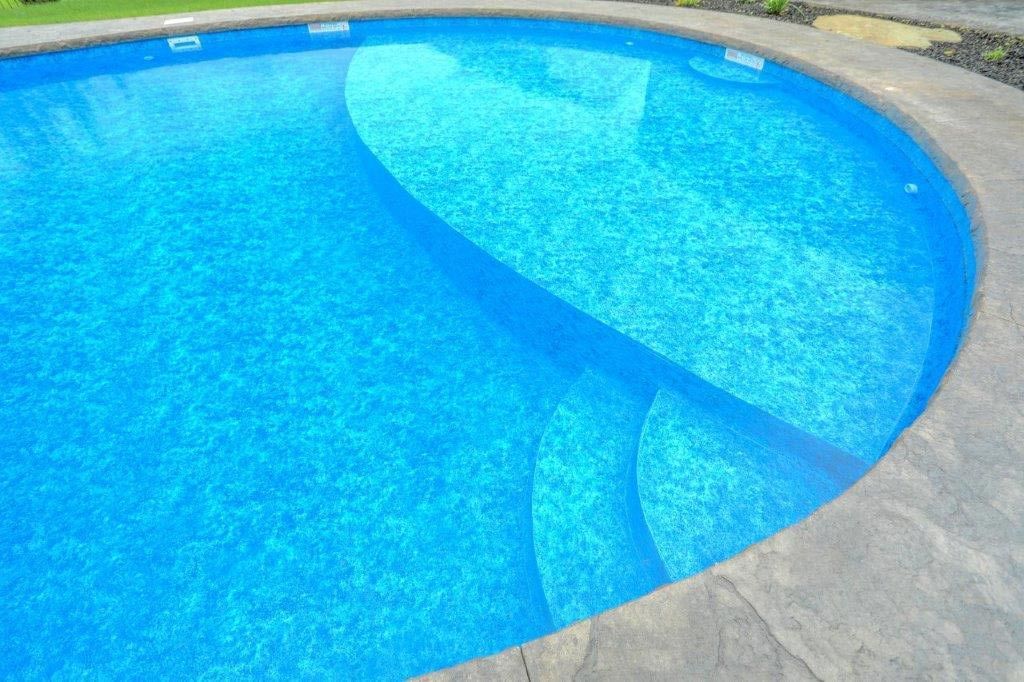 A blue swimming pool with a stone border and steps