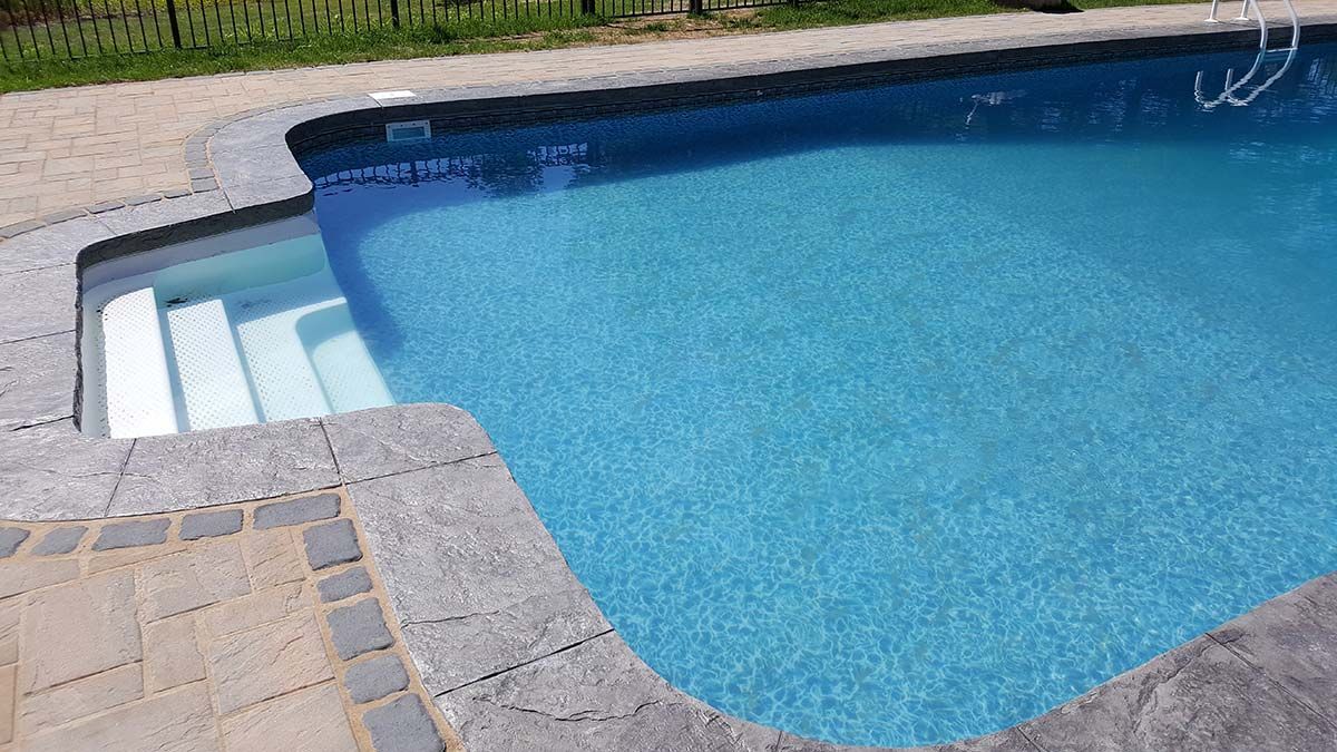 A large swimming pool filled with blue water is sitting on top of a stone patio.