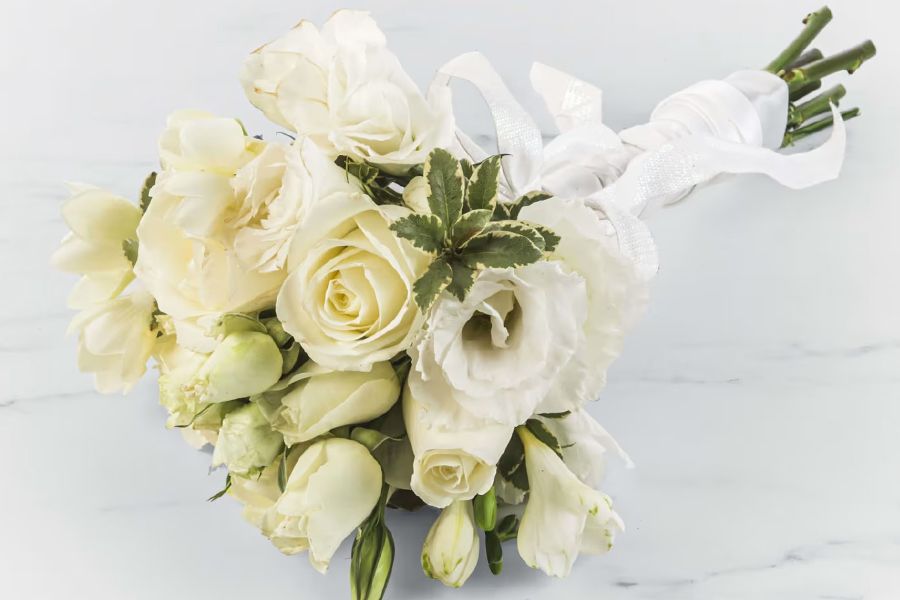 White rose bouquet tied with a white ribbon, on a white marbled surface.