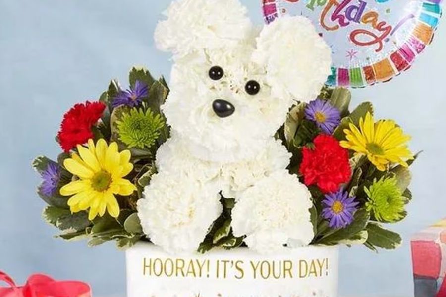 Floral arrangement shaped as a white dog, surrounded by colorful flowers, with a 