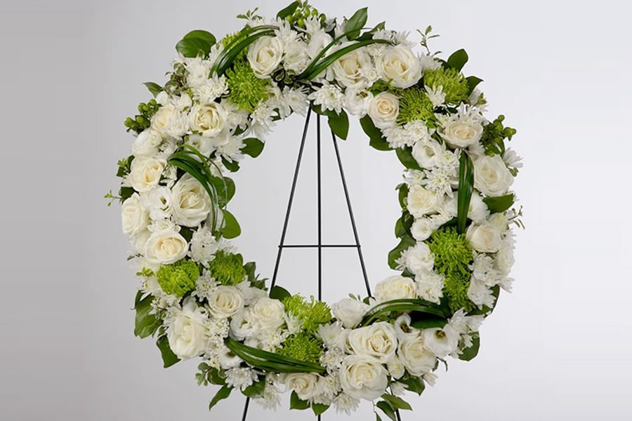 A floral wreath of white roses and green accents on a black stand, likely for a memorial.