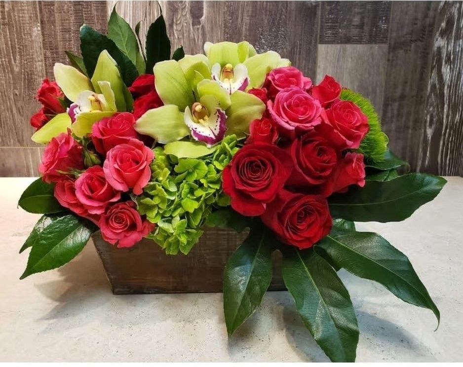 A wooden box filled with red roses and green orchids