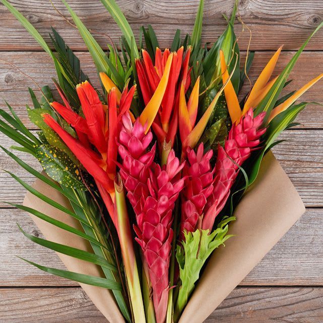 A bouquet of tropical flowers wrapped in brown paper on a wooden table