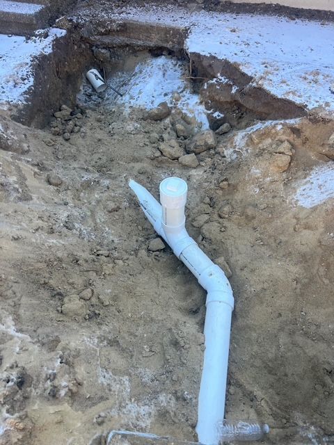A white pipe is laying in the dirt in a hole.