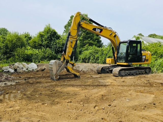 A yellow cat excavator is working on a dirt field.