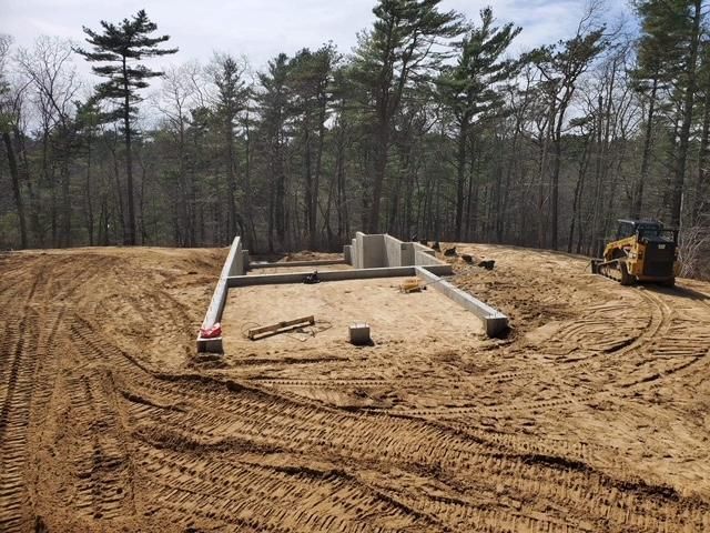 A bulldozer is driving through a dirt field with trees in the background.