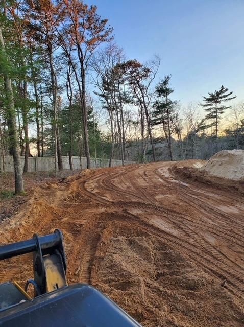 A tractor is driving down a dirt road in the woods.