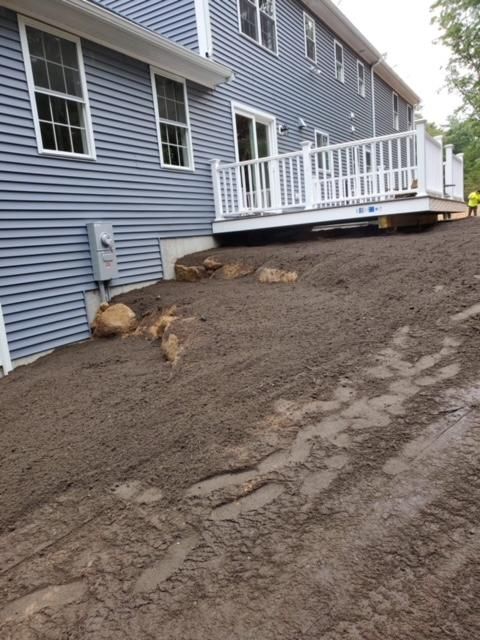 A blue house with a white deck is sitting on a dirt road.