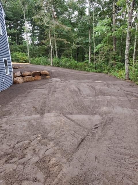 A dirt road leading to a house with trees in the background.