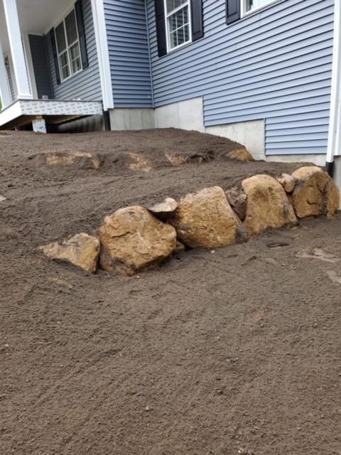 A row of rocks sitting on top of a dirt hill in front of a house.