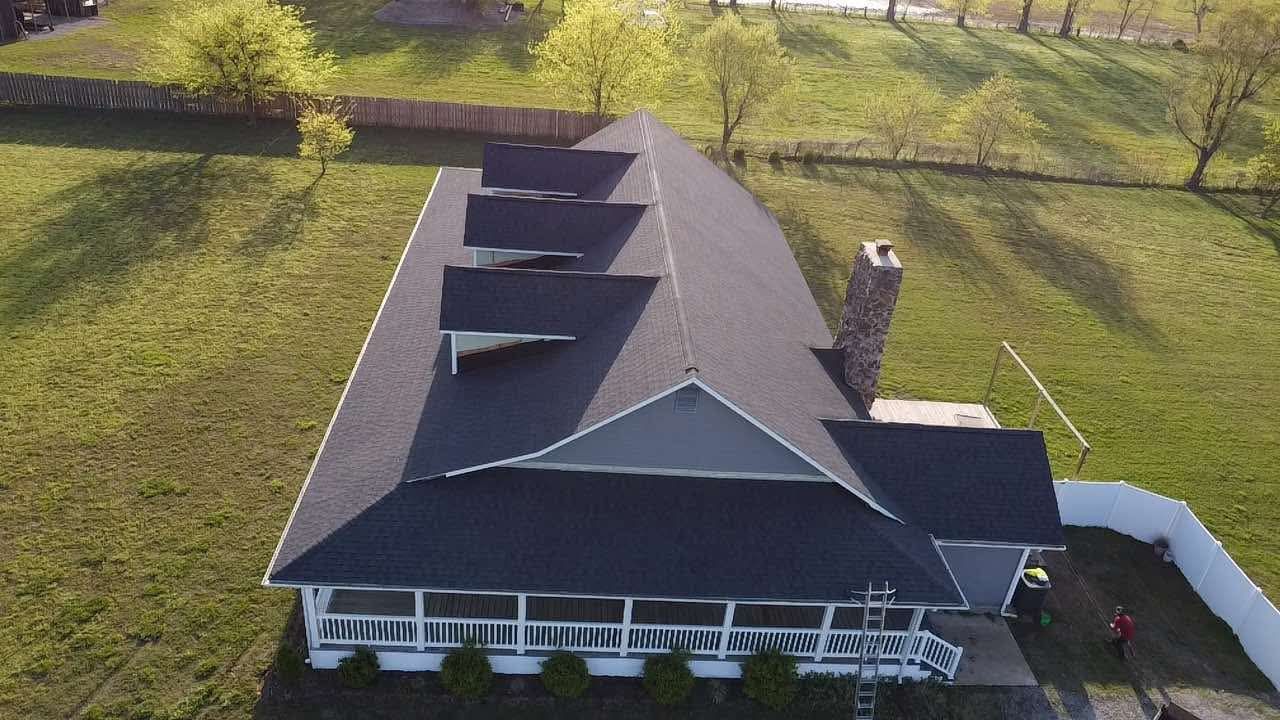 An aerial view of a large house with a black roof surrounded by grass and trees.
