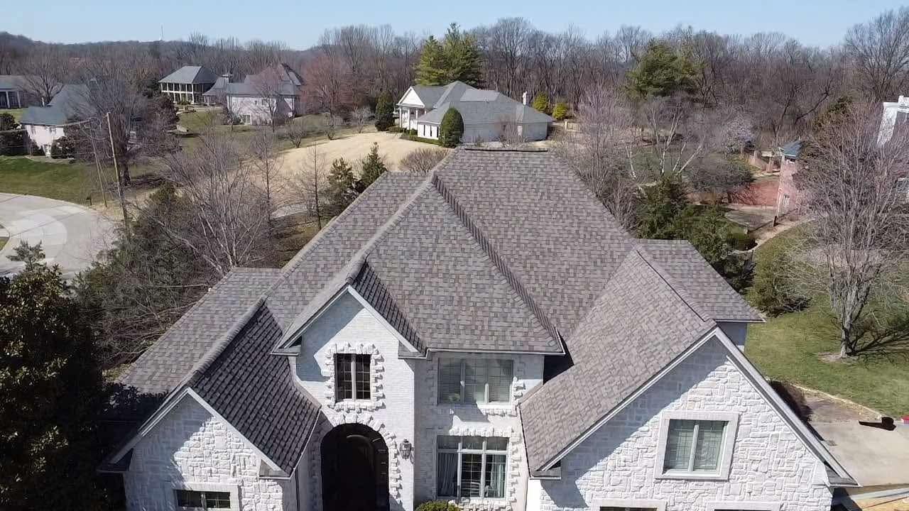 An aerial view of a large white brick house with a gray roof surrounded by trees.