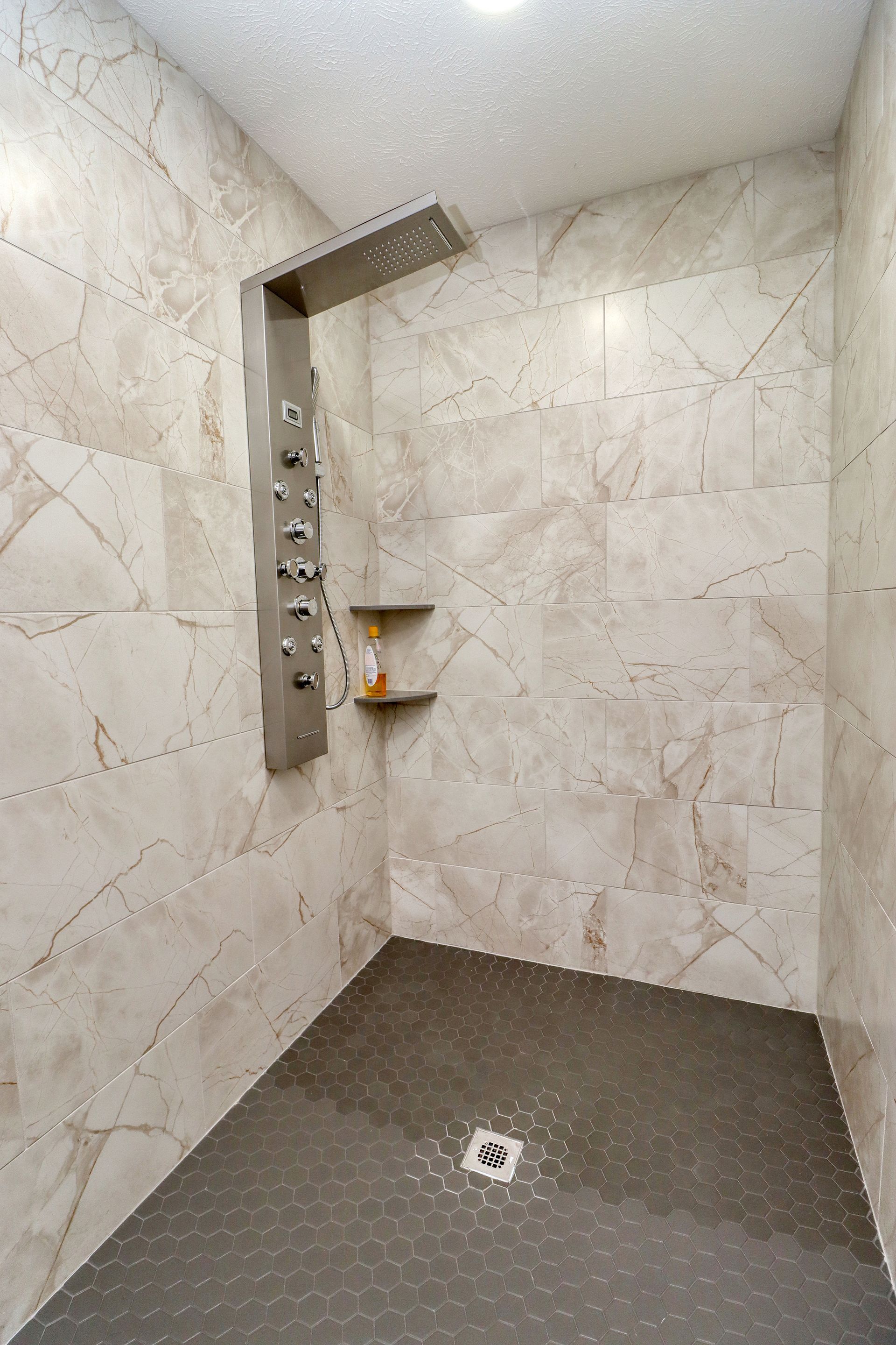 A walk in shower with marble walls and a stainless steel shower head.
