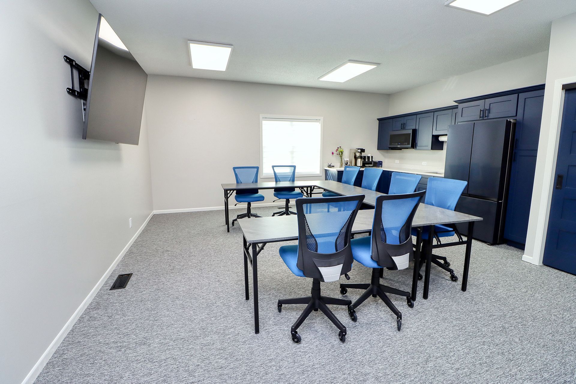 A conference room with tables and chairs and a flat screen tv.