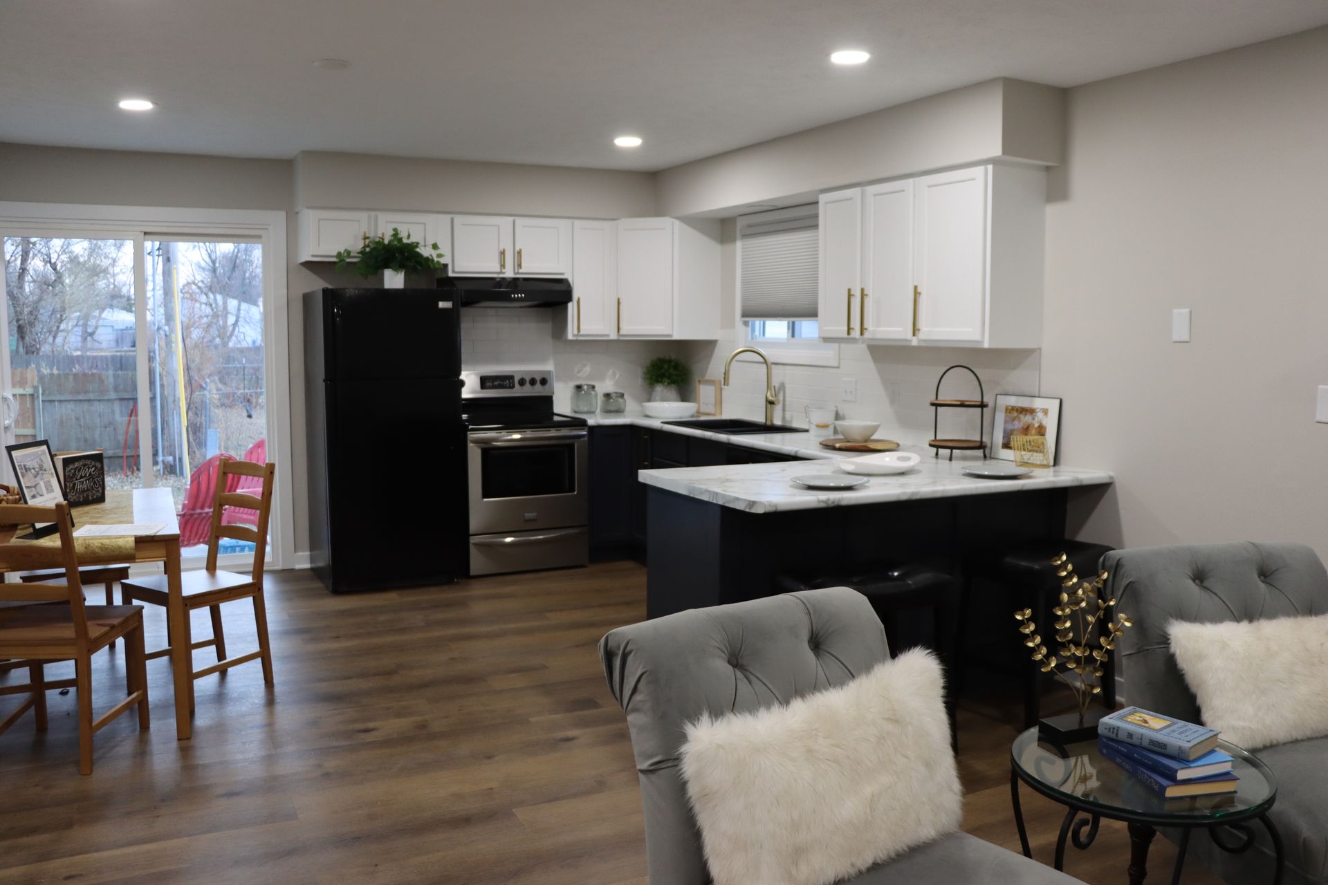 A living room filled with furniture and a kitchen with a black refrigerator.