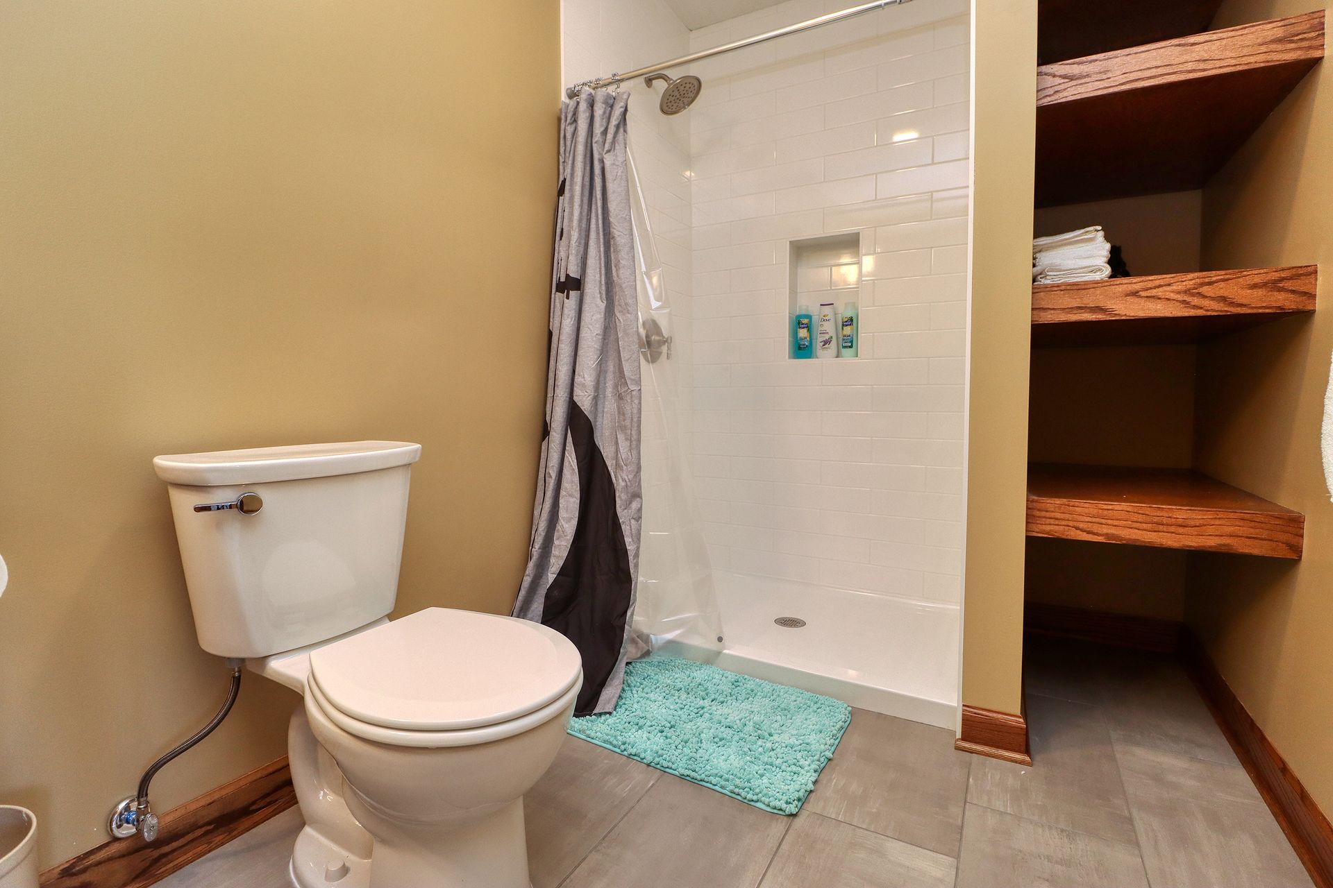 A bathroom with a toilet , shower and shelves.