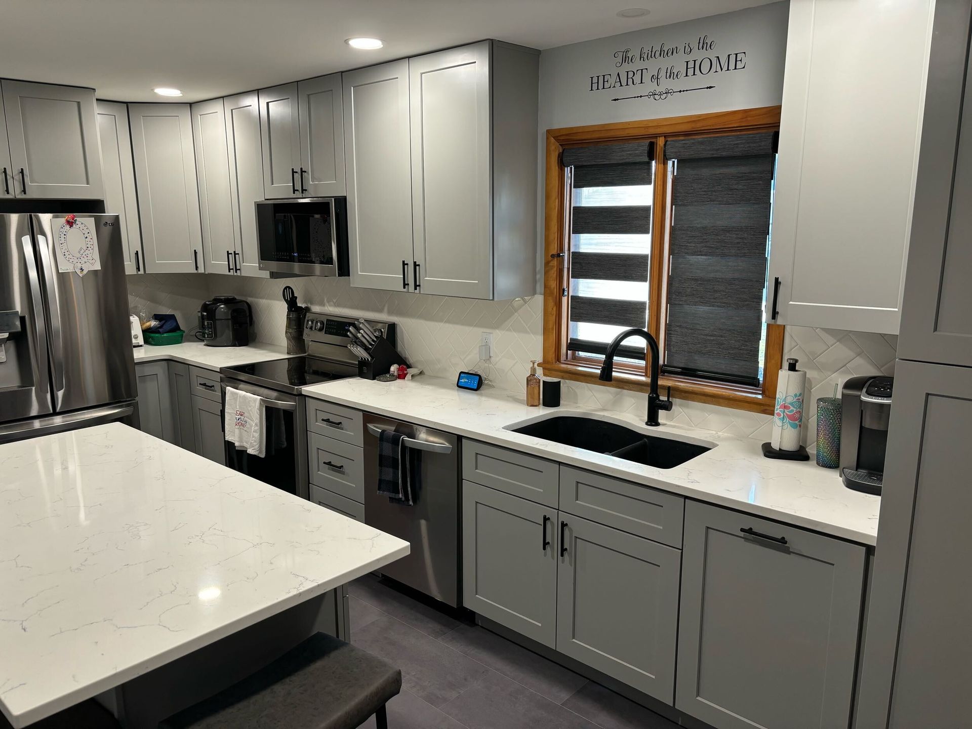 A kitchen with gray cabinets , white counter tops , stainless steel appliances and a large island.