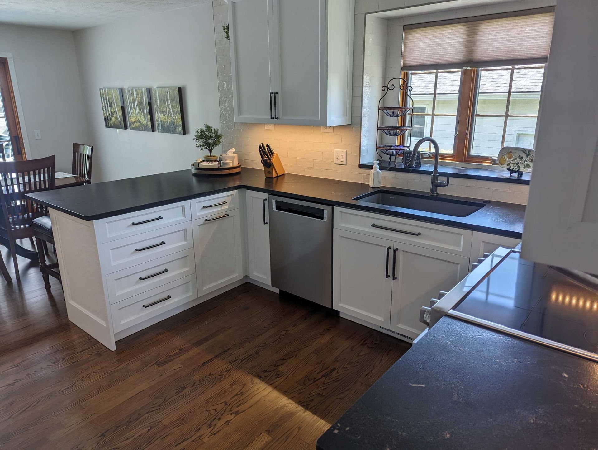 A kitchen with white cabinets , black counter tops , a sink and a dishwasher.