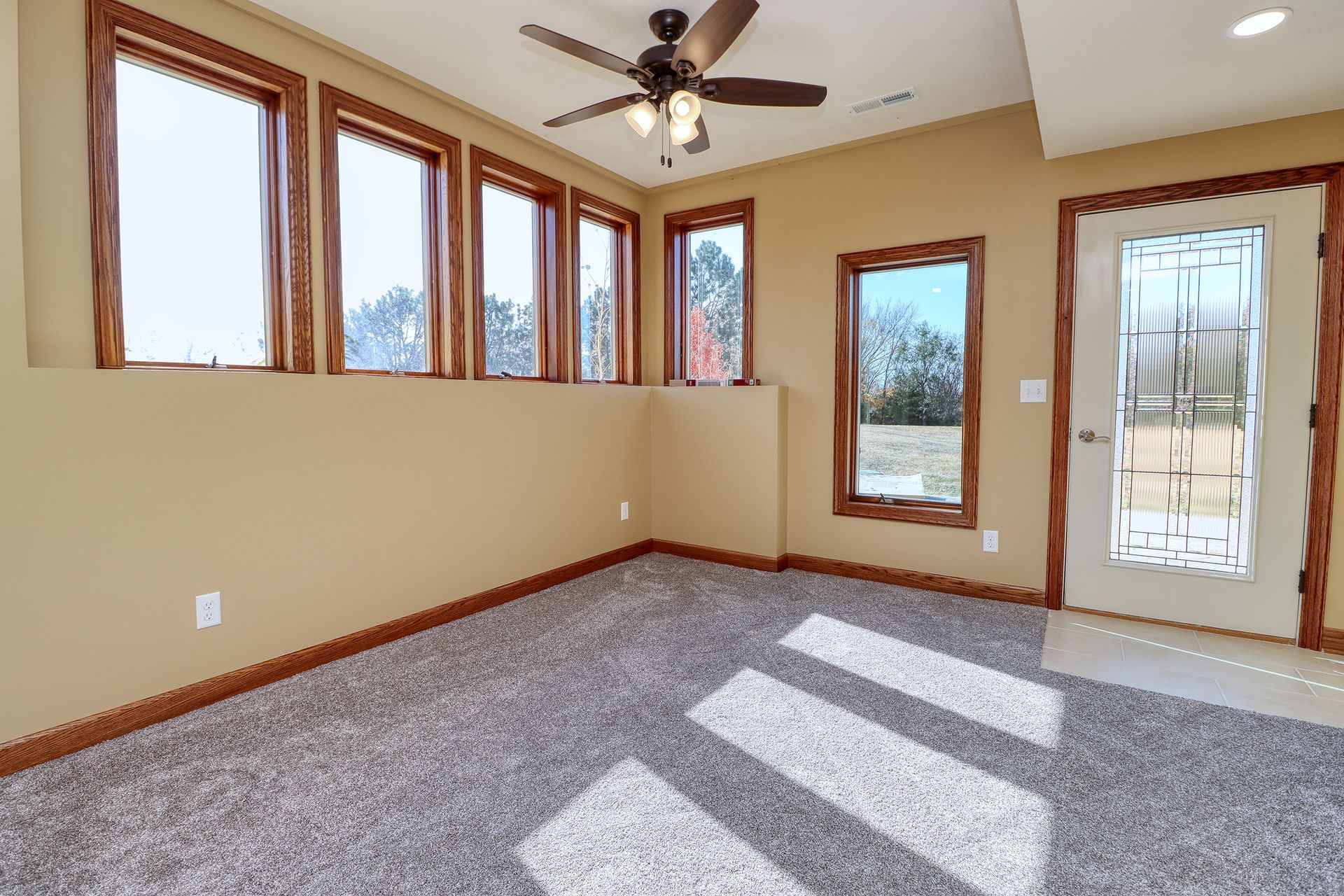 An empty room with a lot of windows and a ceiling fan.