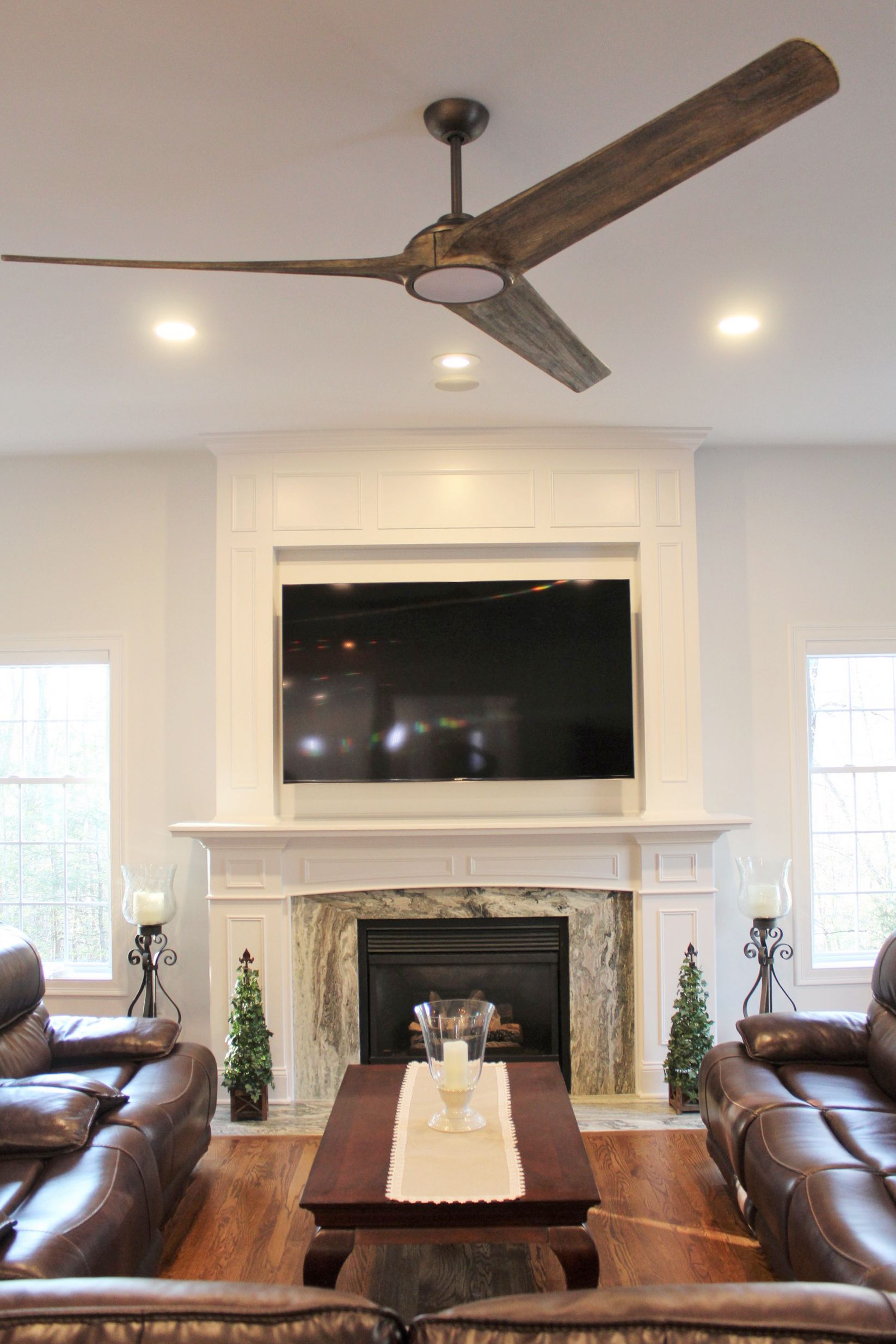 a living room with a fireplace, ceiling fan, and flat screen tv
