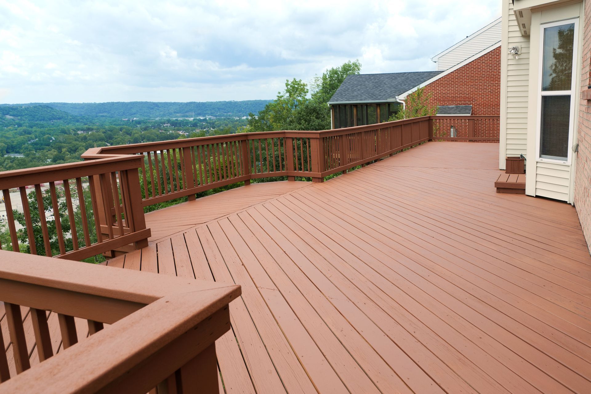 Wooden deck overlooking a scenic valley with a brown railing, and part of a house.