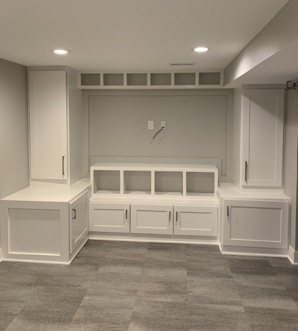 Built-in white storage unit with cabinets and shelves on a gray wall; a gray floor.