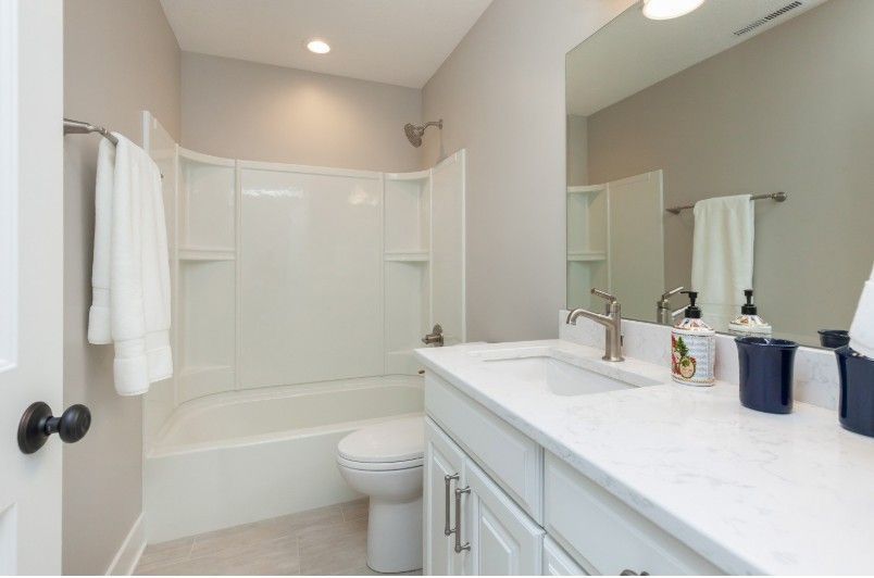 Bathroom with white tub/shower, vanity, and toilet; light gray walls; white towels.