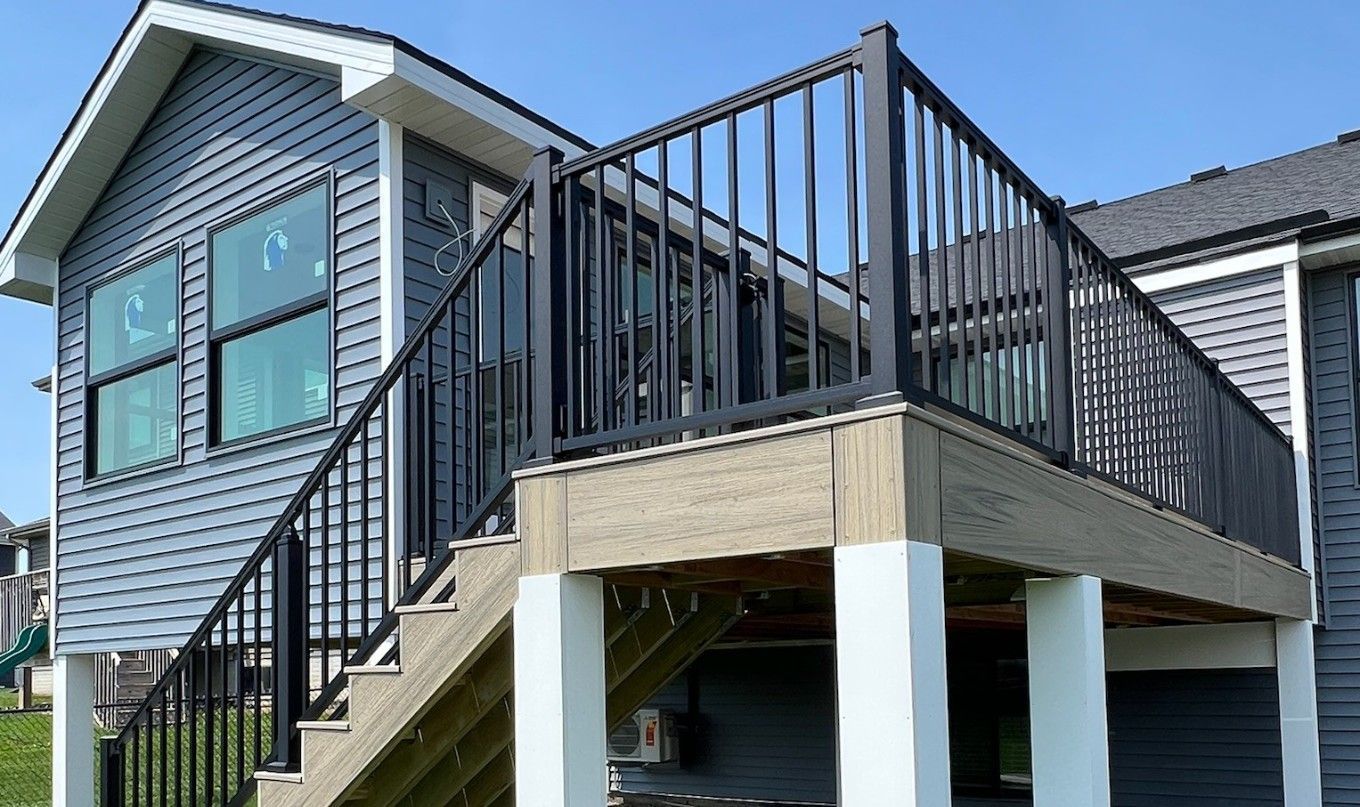 Wooden deck with table and chairs, overlooking trees and a body of water under a blue sky.