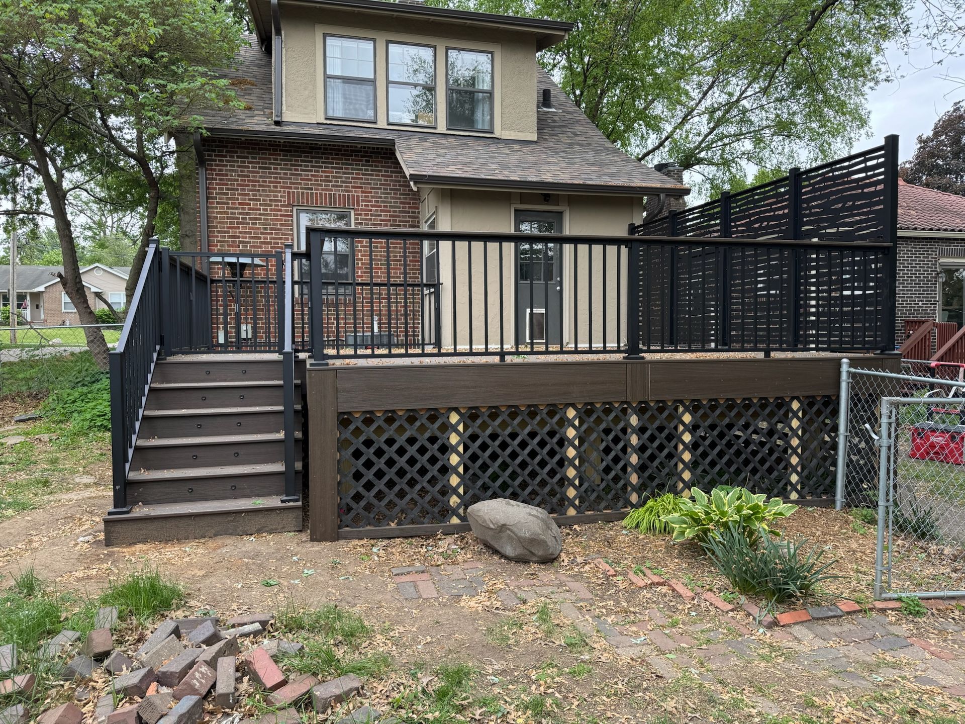 Backyard deck with dark railing and latticework skirting. House in background.
