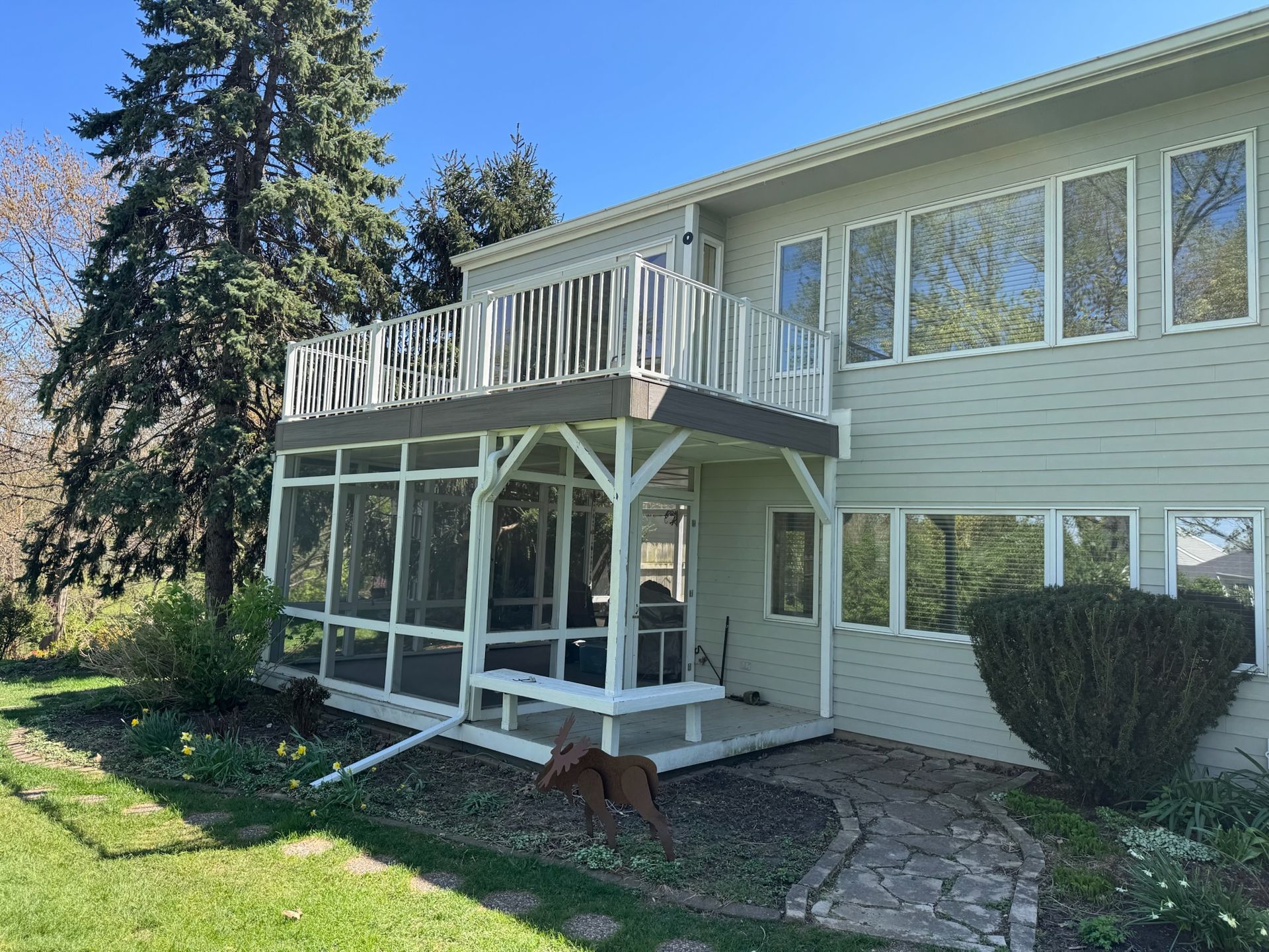 Two-story house with a screened-in porch and deck. A dog sits on the grass.