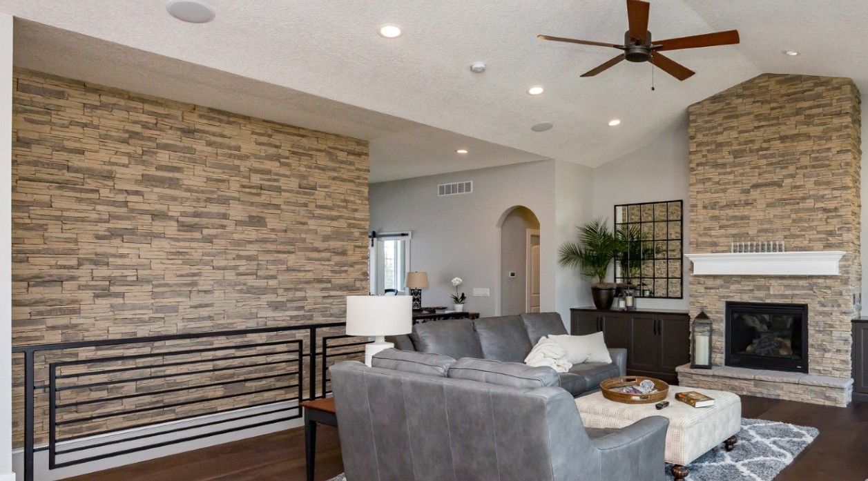 Living room with stone accent walls, gray sectional sofa, fireplace, and ceiling fan.