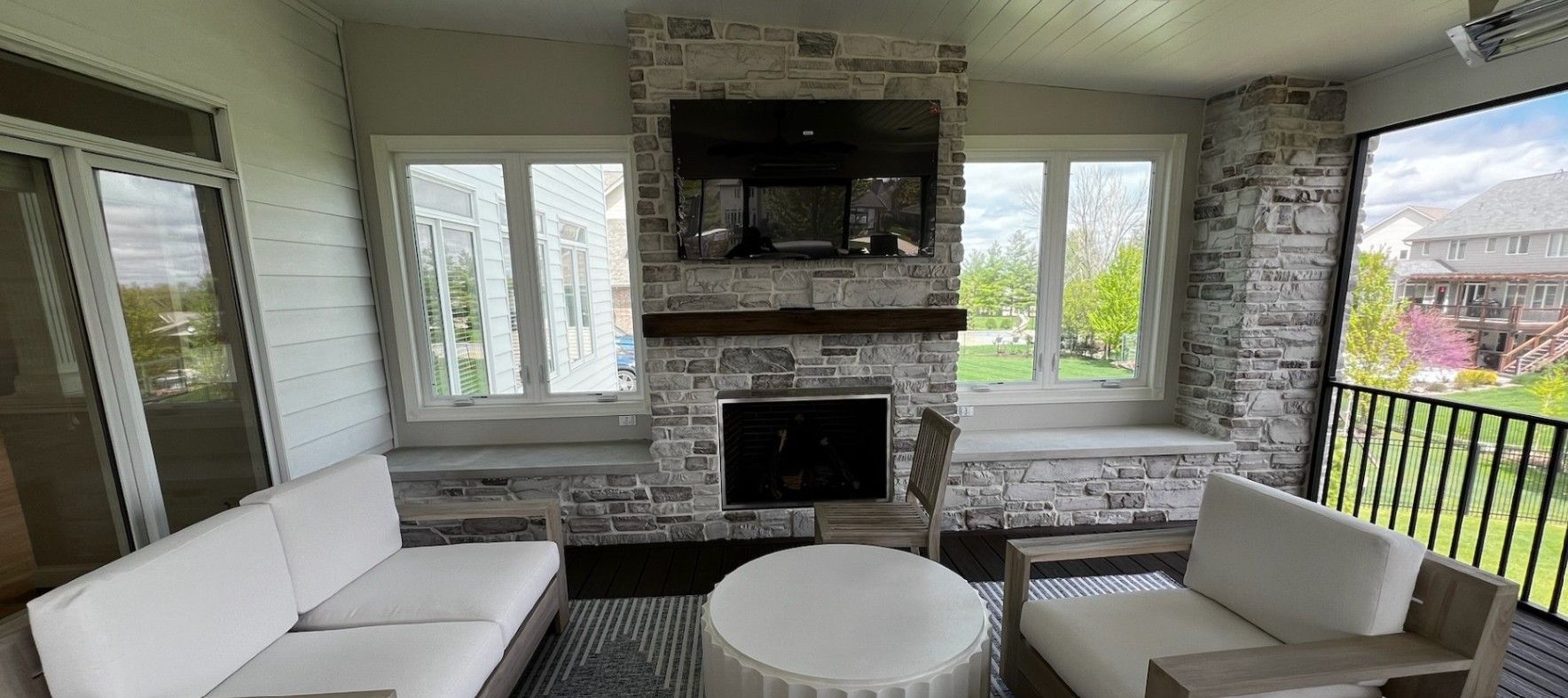 A screened-in porch with a fireplace, TV, and outdoor furniture.