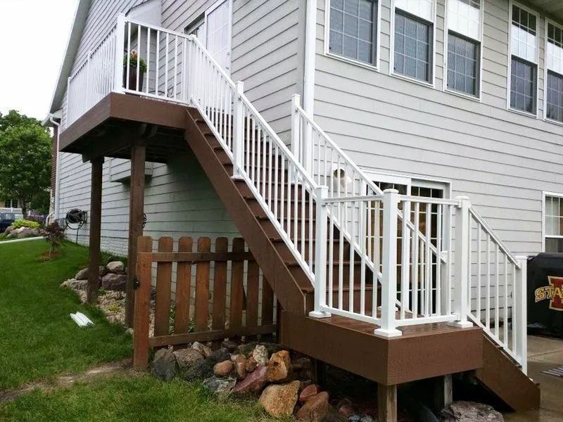 White-railed deck with stairs attached to a light gray house. Brown deck and stair surfaces, small wooden fence below.