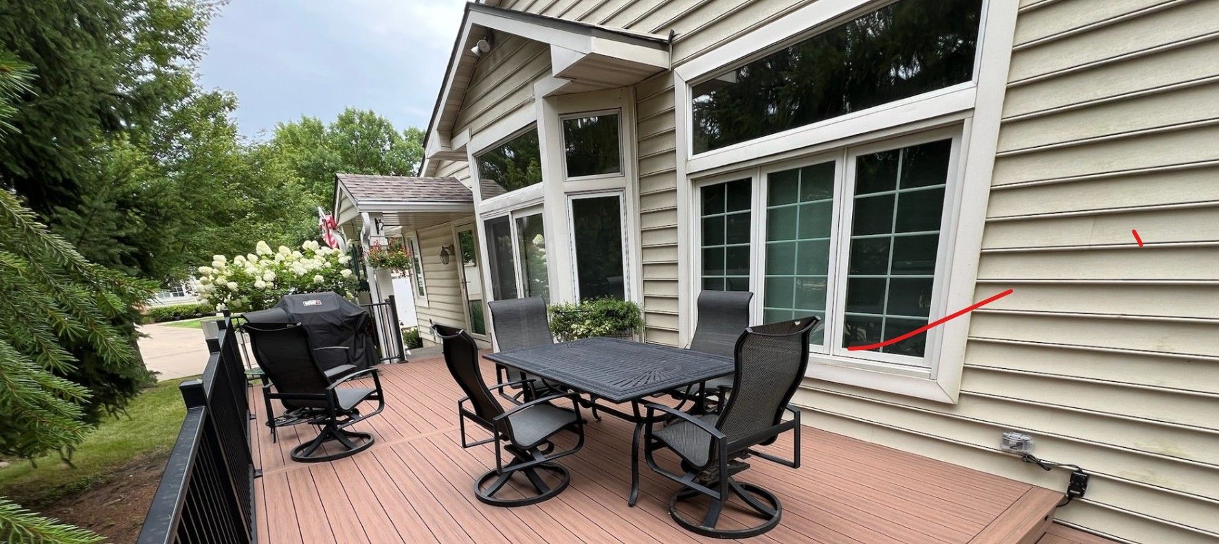 Patio with a table and chairs, adjacent to a house with large windows and tan siding.