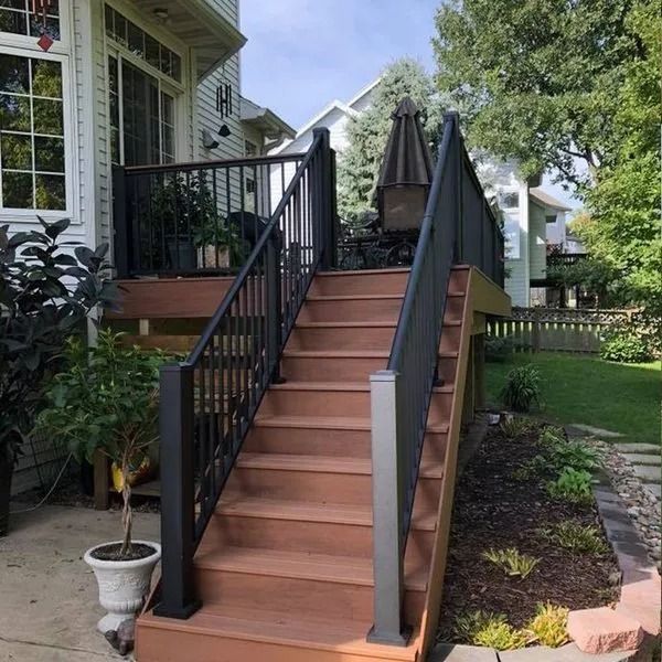 Wooden deck stairs with black railings leading up to a raised deck with an umbrella and backyard view.