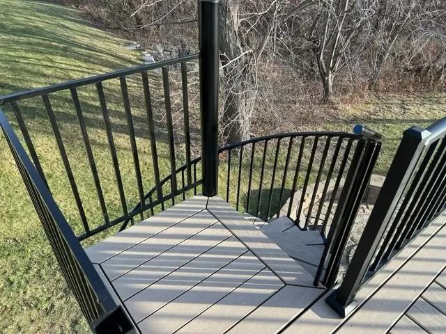 Black metal deck railing with composite wood flooring, overlooking a green yard and trees.