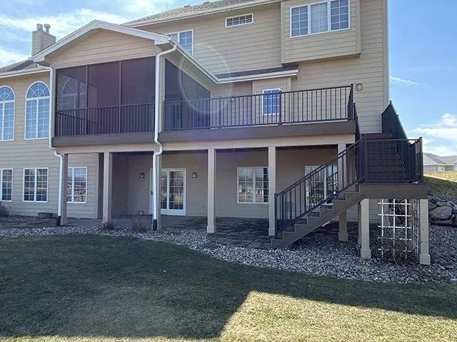 Back view of a light beige two-story house with a wooden deck and screened porch.