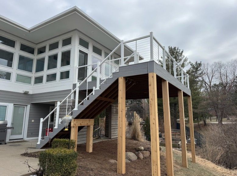 Gray deck with white railing and stairs attached to a house with many windows.