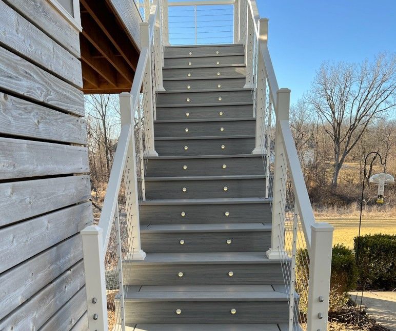 Gray wooden outdoor staircase with white railings, against a blue sky.